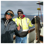 Two men on a boat holding up a fish.