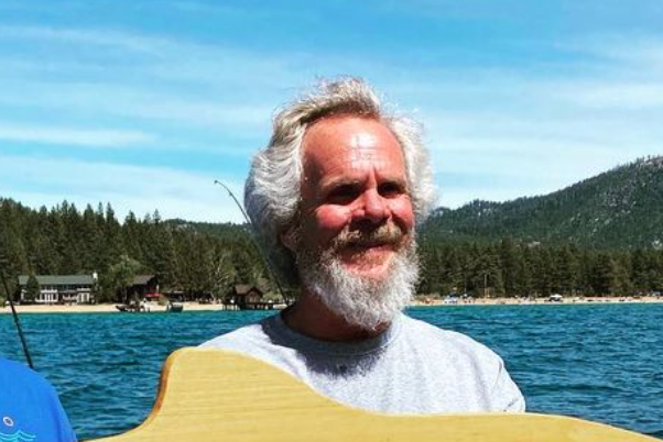 A man with white beard and long hair in front of the ocean.