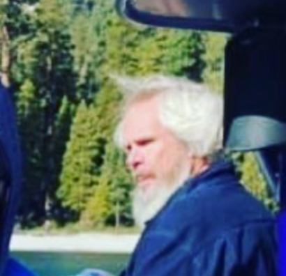 A man with white hair and beard sitting in the back of a truck.